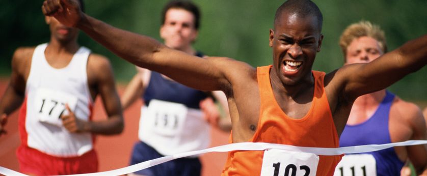 Track runner crossing finish line ahead of other racers.